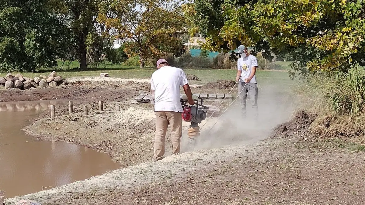 Operarios compactando el terreno en la costa de una laguna en obra
